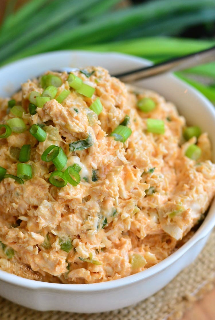 Zesty Buffalo Chicken Salad in a white bowl with green onions on top with a spoon 