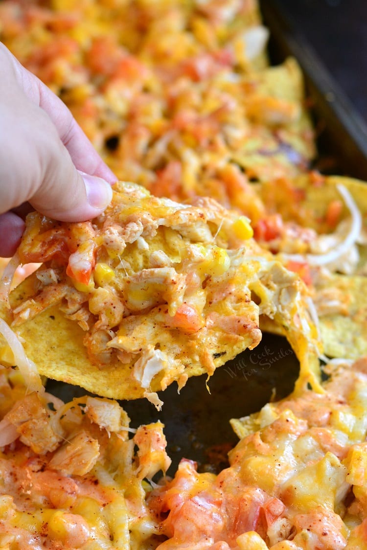 Holding a nacho in my hand with the sheet pan of nachos in the background.