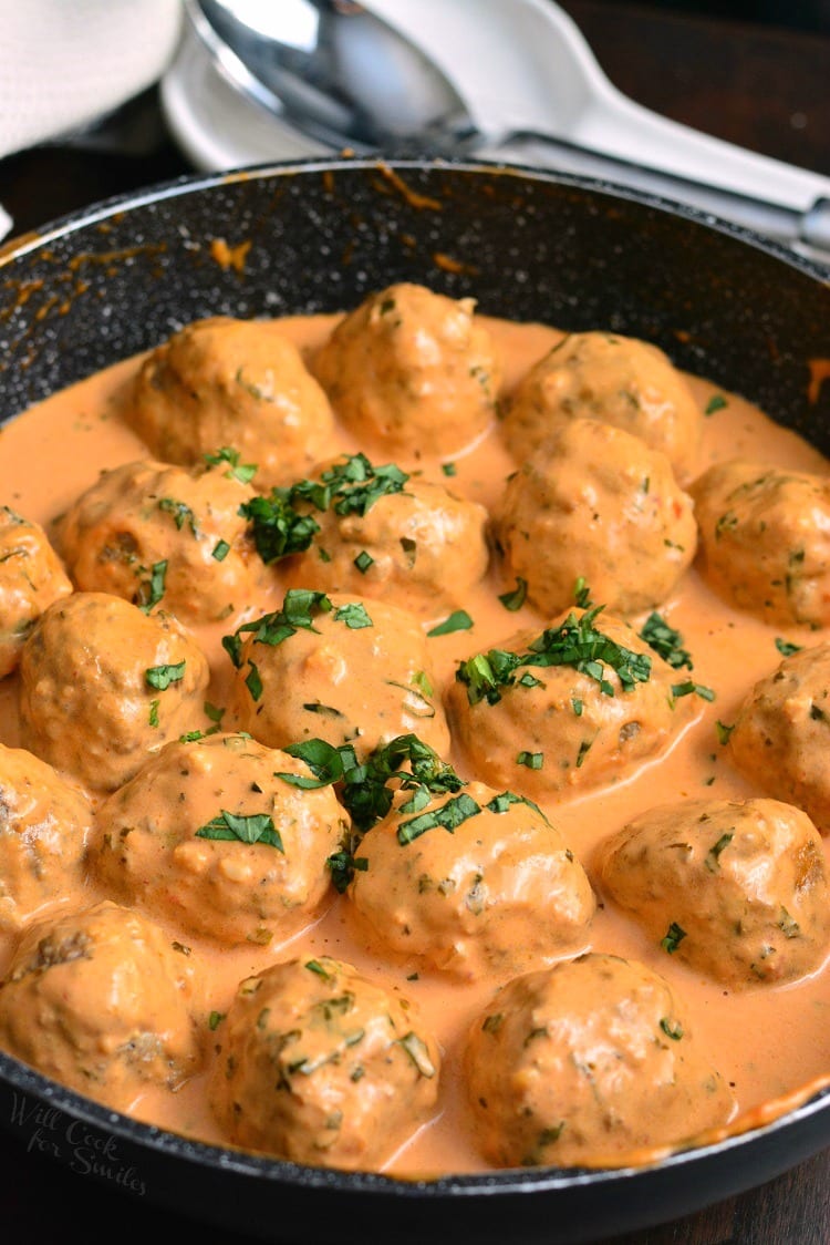 Creamy Tomato Basil Meatballs in a pan with a spoon in the background 