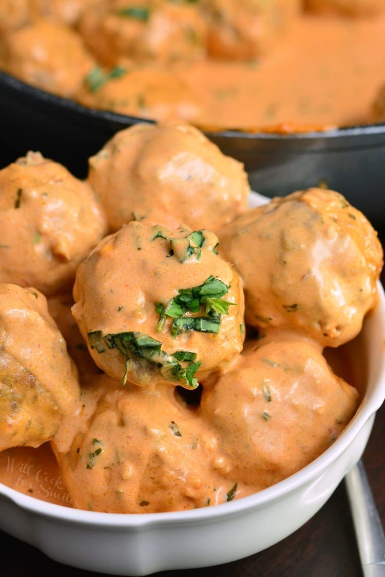 Creamy Tomato Basil Meatballs in a bowl with the pan of meatballs in the background 