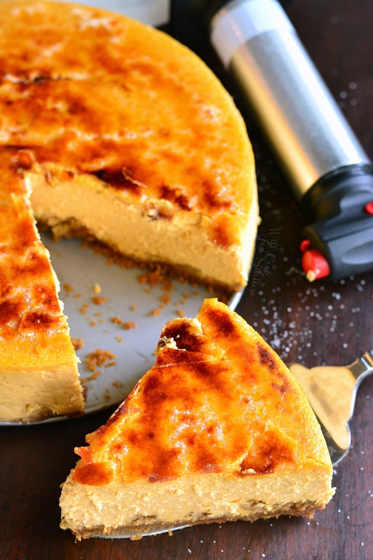 slice of Creme Brulee Pumpkin Cheesecake on a table with rest of the cheesecake on the table with the torch 