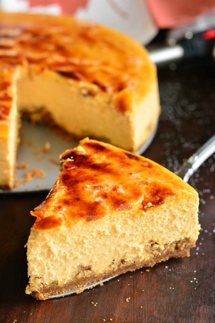 Creme Brulee Pumpkin Cheesecake slice on a table with the rest of the cheesecake in the background 