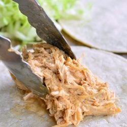Putting shredded chicken on a soft tortilla with tongs.