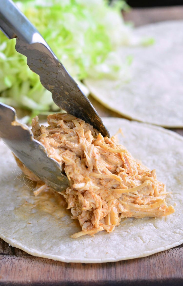 Putting shredded chicken on a soft tortilla with tongs.