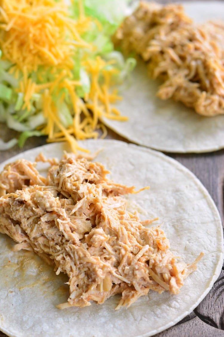 Crock Pot Creamy Pulled Chicken Tacos on a cutting board with lettuce and cheese in the background 