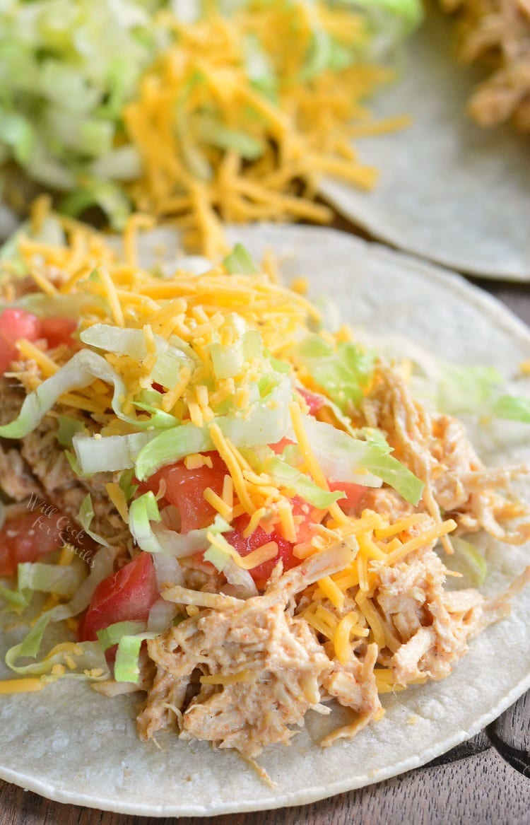 Pulled chicken taco on a tortilla with lettuce, tomato, and cheese on a wooden cutting board.