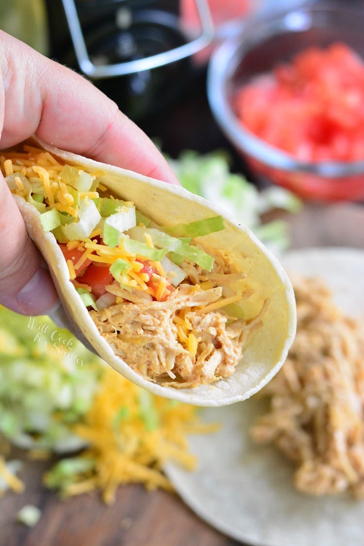 holding a soft taco with shredded chicken, lettuce, tomato, and cheese.