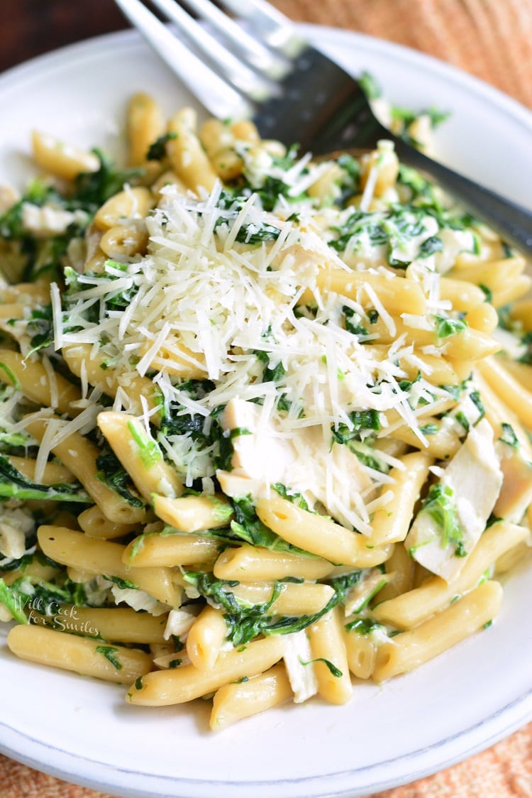 Garlic and Spinach Alfredo Chicken Pasta in a bowl with shredded cheese on top with fork 