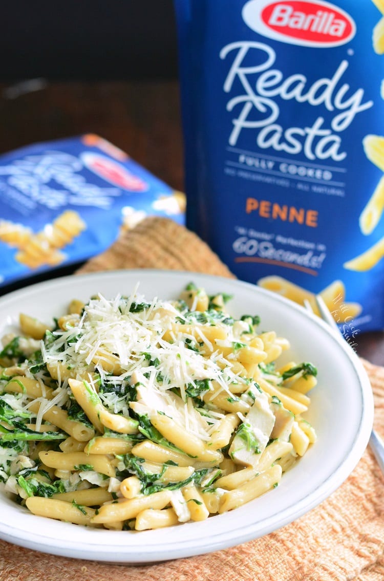 Garlic and Spinach Alfredo Chicken Pasta with cheese on top in a bowl on a kitchen towel with the bag of pasta in the background 