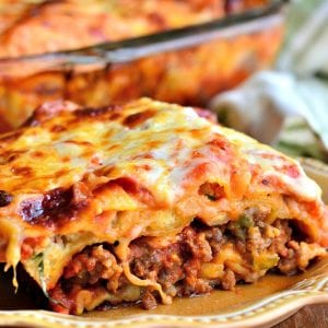 a slice of Italian sausage lasagna on a brown plate next to the whole lasagna.