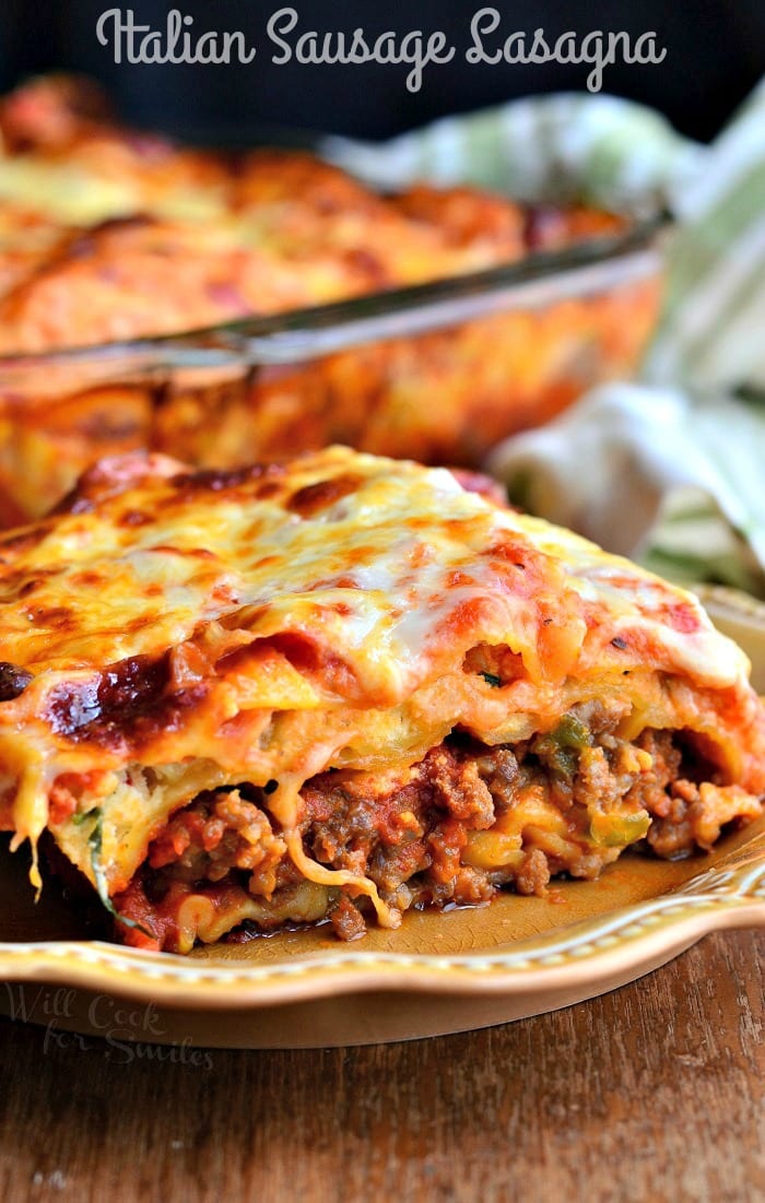 italian sausage lasagna on a plate with the rest of the lasagna in a casserole dish behind it 