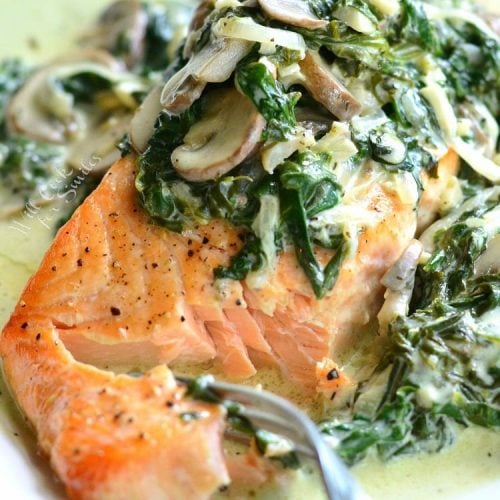 salmon Florentine with spinach and mushroom on a plate with bite of spinach on a fork.