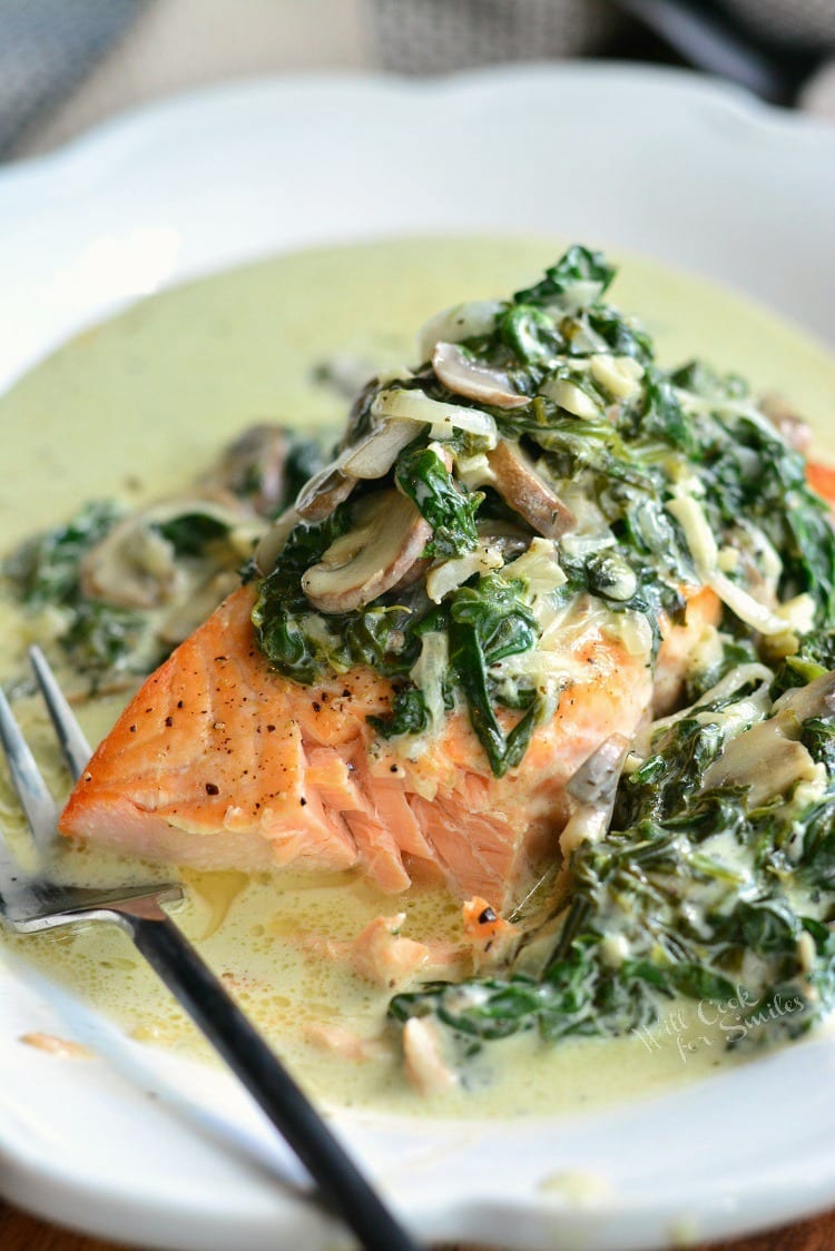 salmon Florentine with spinach and mushrooms with a bite cut out of it and on a white plate.  