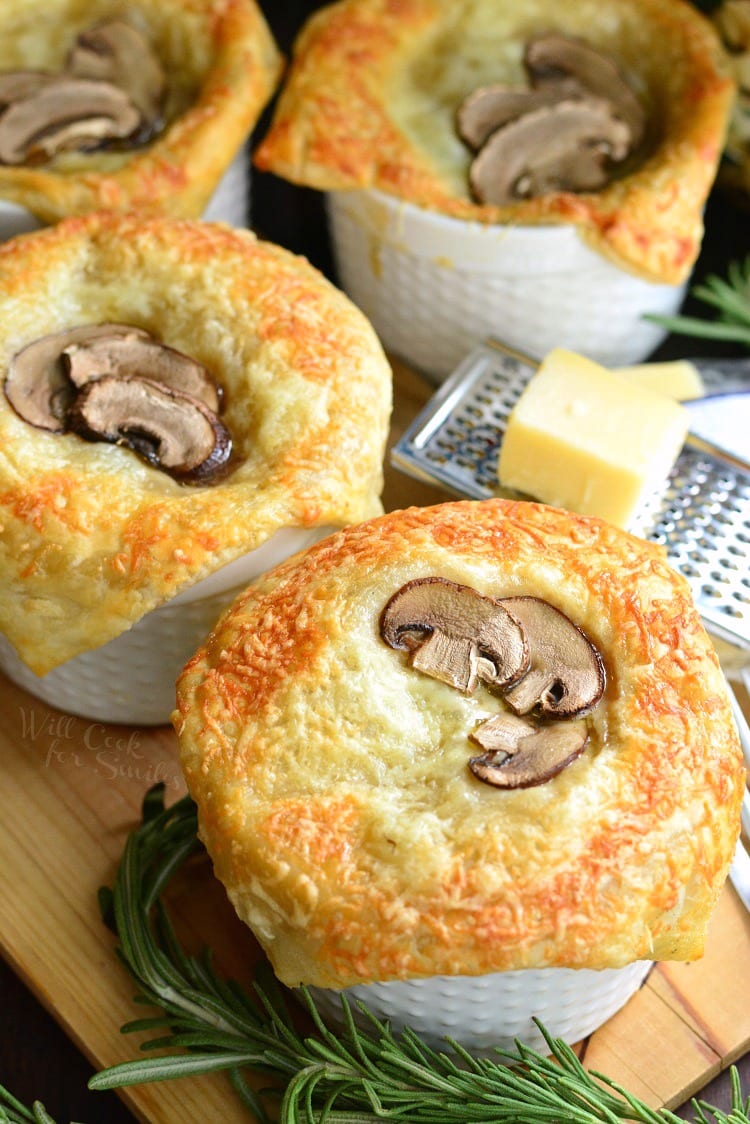 Individual Creamy Chicken and Mushroom Pot Pies with rosemary on a cutting board with cheese on top of a cheese grater on a wood cutting board 