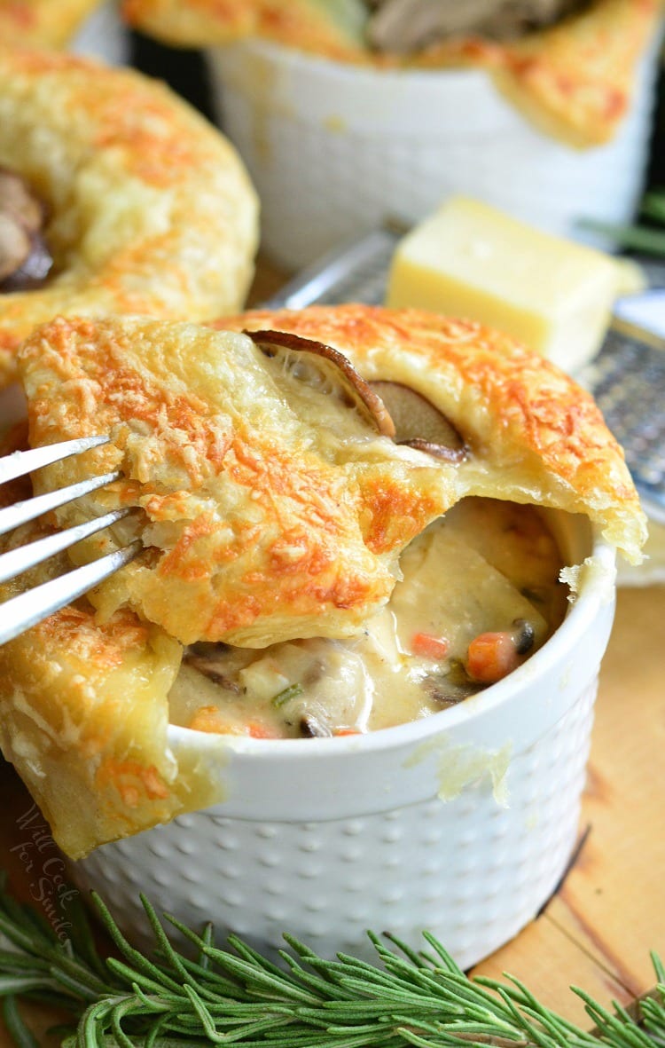 Individual Creamy Chicken and Mushroom Pot Pies with a fork with rosemary on a cutting board with cheese on top of a cheese grater on a wood cutting board 