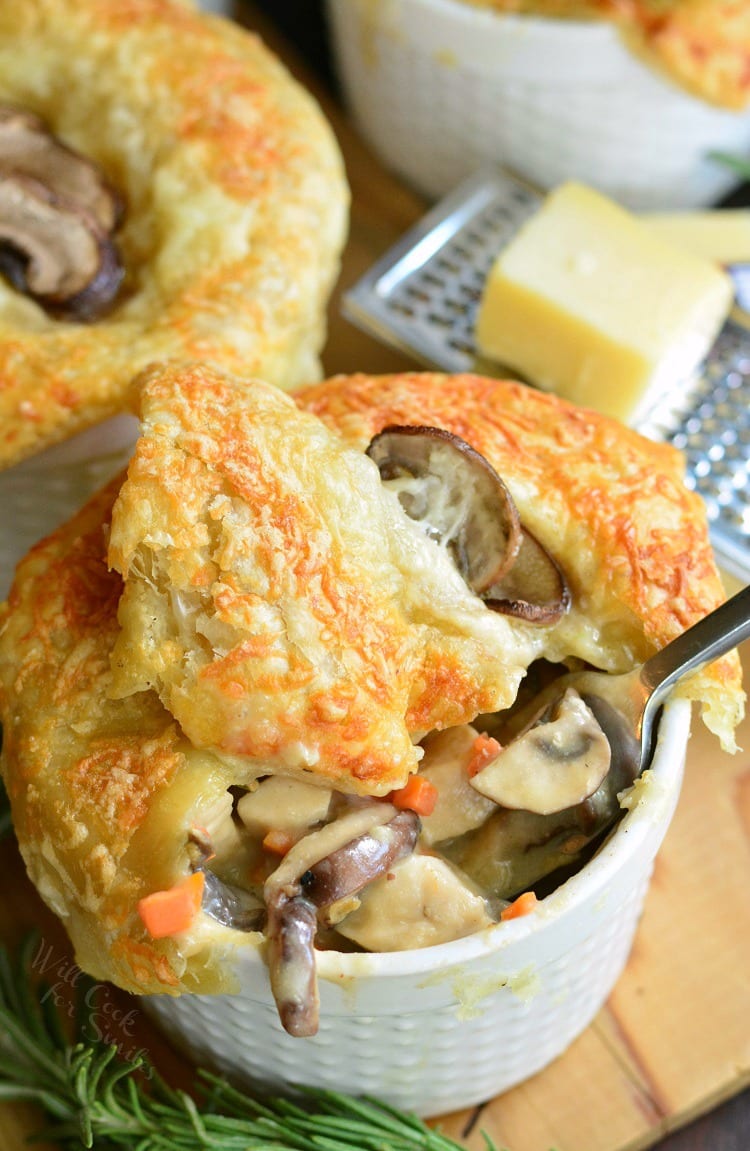 Individual Creamy Chicken and Mushroom Pot Pies with a fork with rosemary on a cutting board with cheese on top of a cheese grater on a wood cutting board 