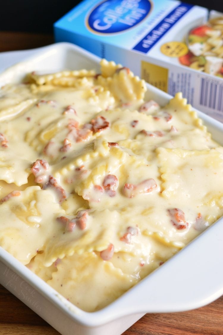 Baked Ravioli Mac and Cheese with Bacon in a white casserole dish with a box of stock in the background on a wood table