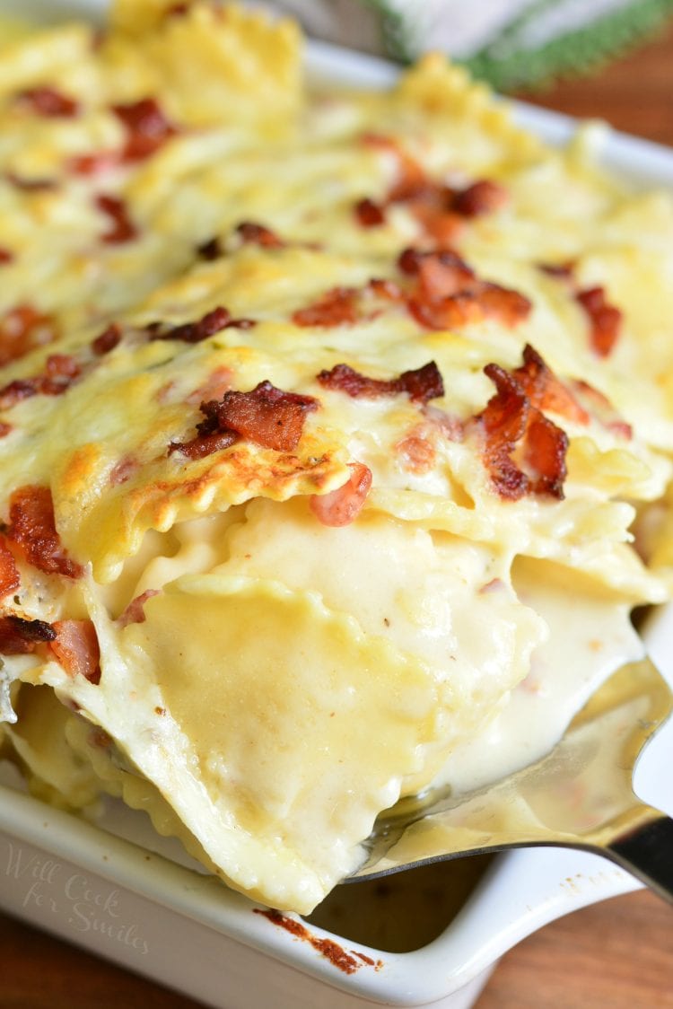 spooning out Baked Ravioli Mac and Cheese with Bacon in a white casserole dish on wood table