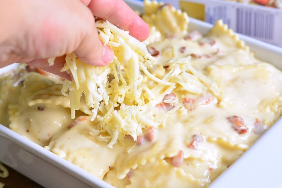 sprinking cheese over Ravioli Mac and Cheese with Bacon that is in a white casserole dish 