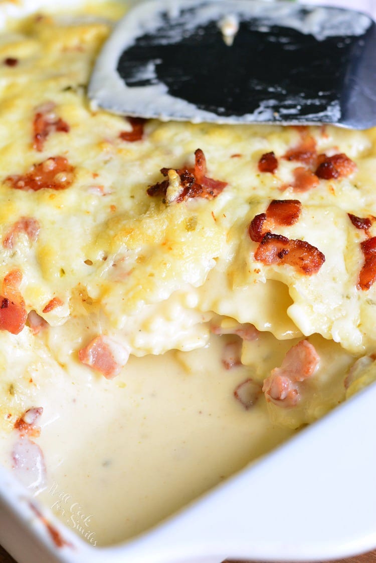 Baked Ravioli Mac and Cheese with Bacon in a white casserole dish with a spatula on top 