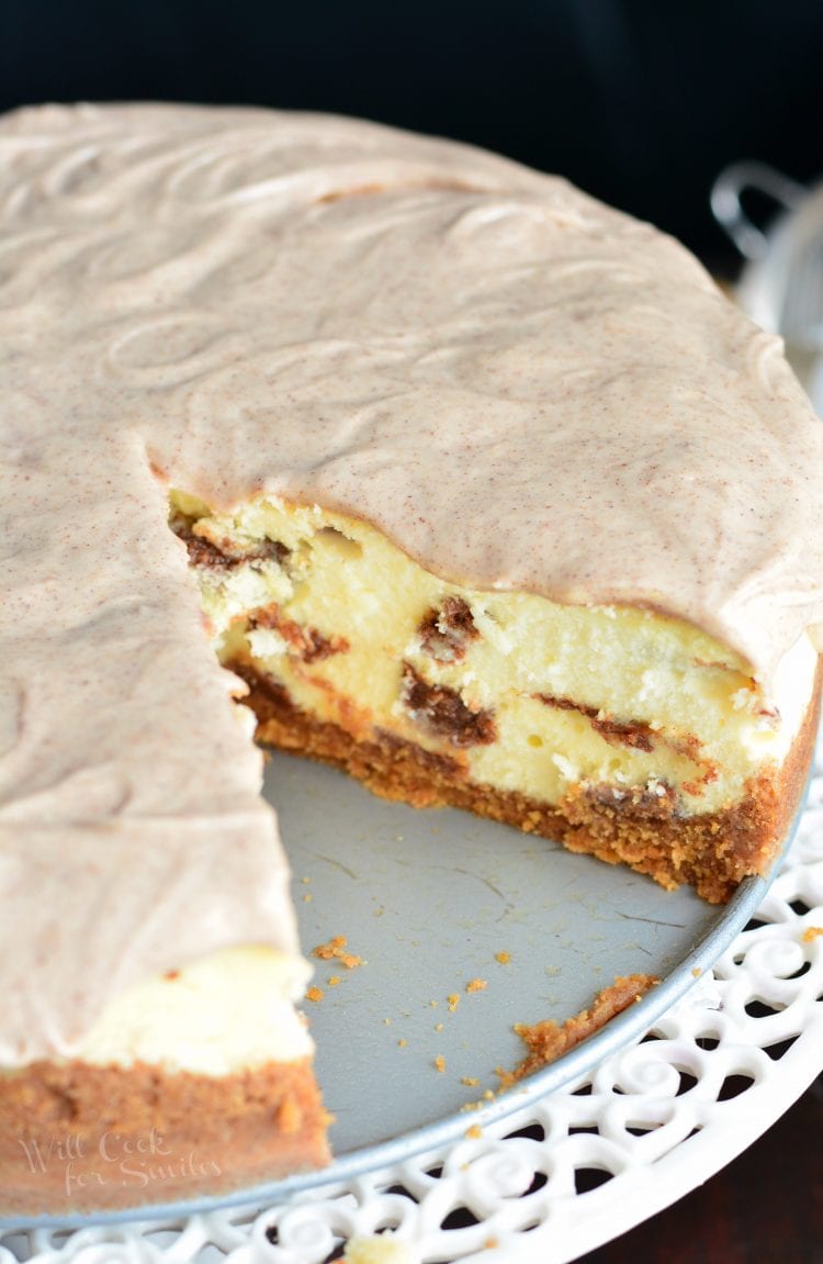 Cinnamon Roll Cheesecake with a slice missing on a cake stand 