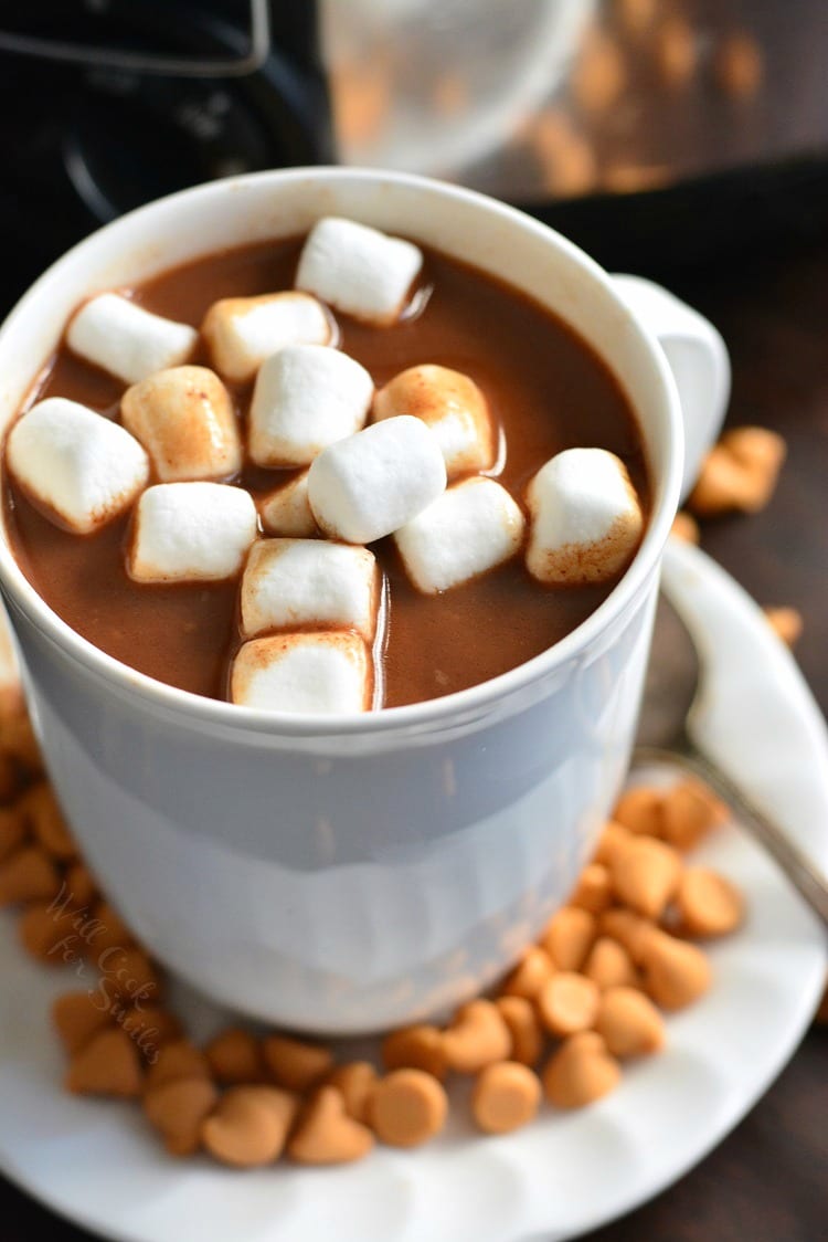 top view of hot chocolate in a white mug topped with mini marshmallows and butterscotch drops on the plate underneath