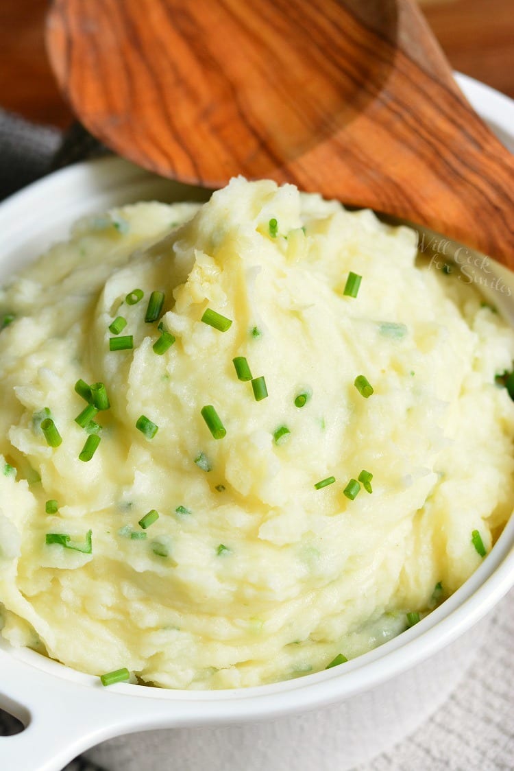 White Cheddar and Chive Creamy Mashed Potatoes in a serving bowl with a wooden serving spoon 