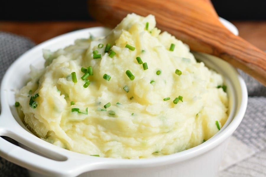 White Cheddar and Chive Creamy Mashed Potatoes in a bowl with a wooden spoon 