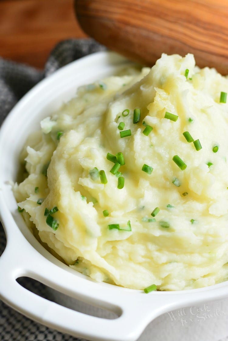 White Cheddar and Chive Creamy Mashed Potatoes in a serving bowl with a wooden spoon 