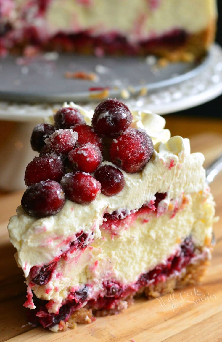 slice of Christmas Cheesecake on a cutting board with rest of cheesecake in background 