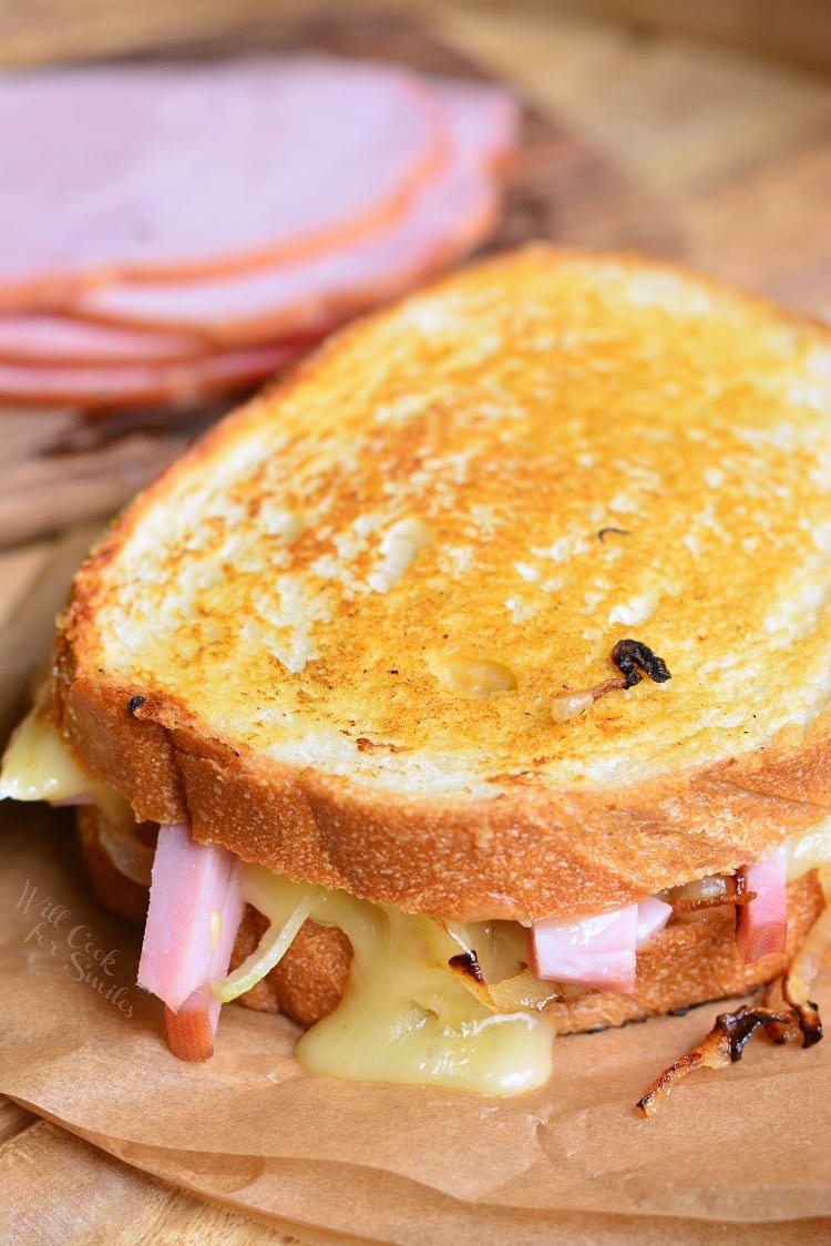 Ham and Brie Grilled Cheese Sandwich on parchment paper on a cutting board with ham in background