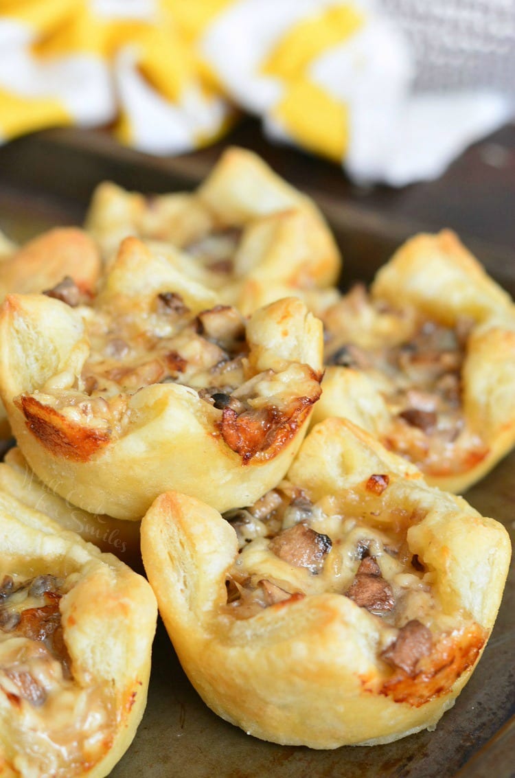 several mushroom puffs baked golden brown stacked on a baking sheet.