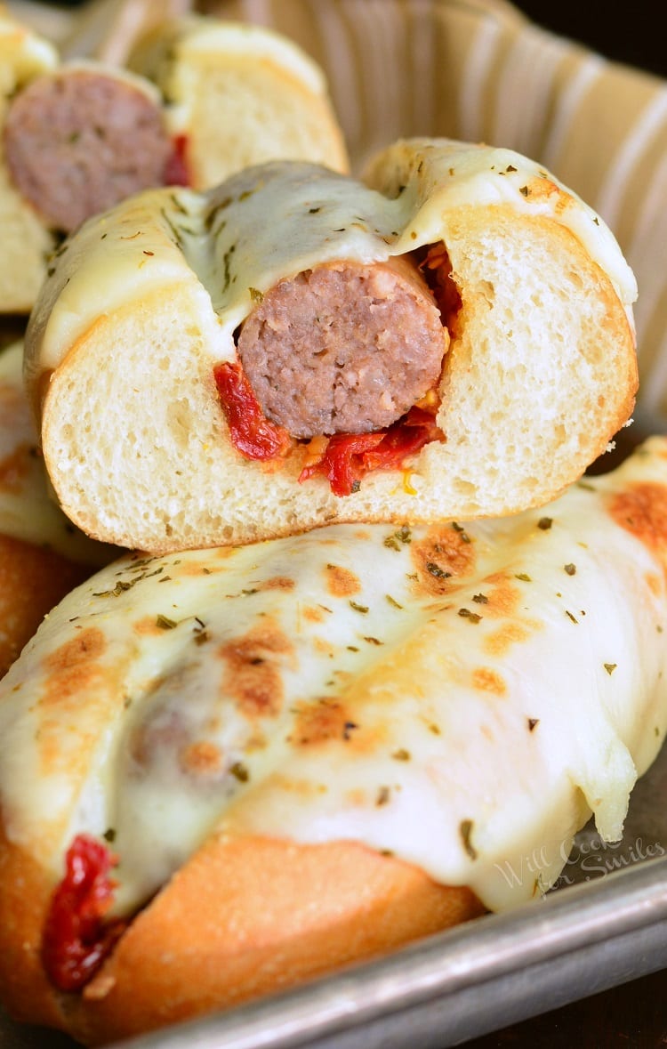 Tomato Mozzarella Italian Sausage Hoagies stacked on top of each other with one cut in half on a baking sheet 