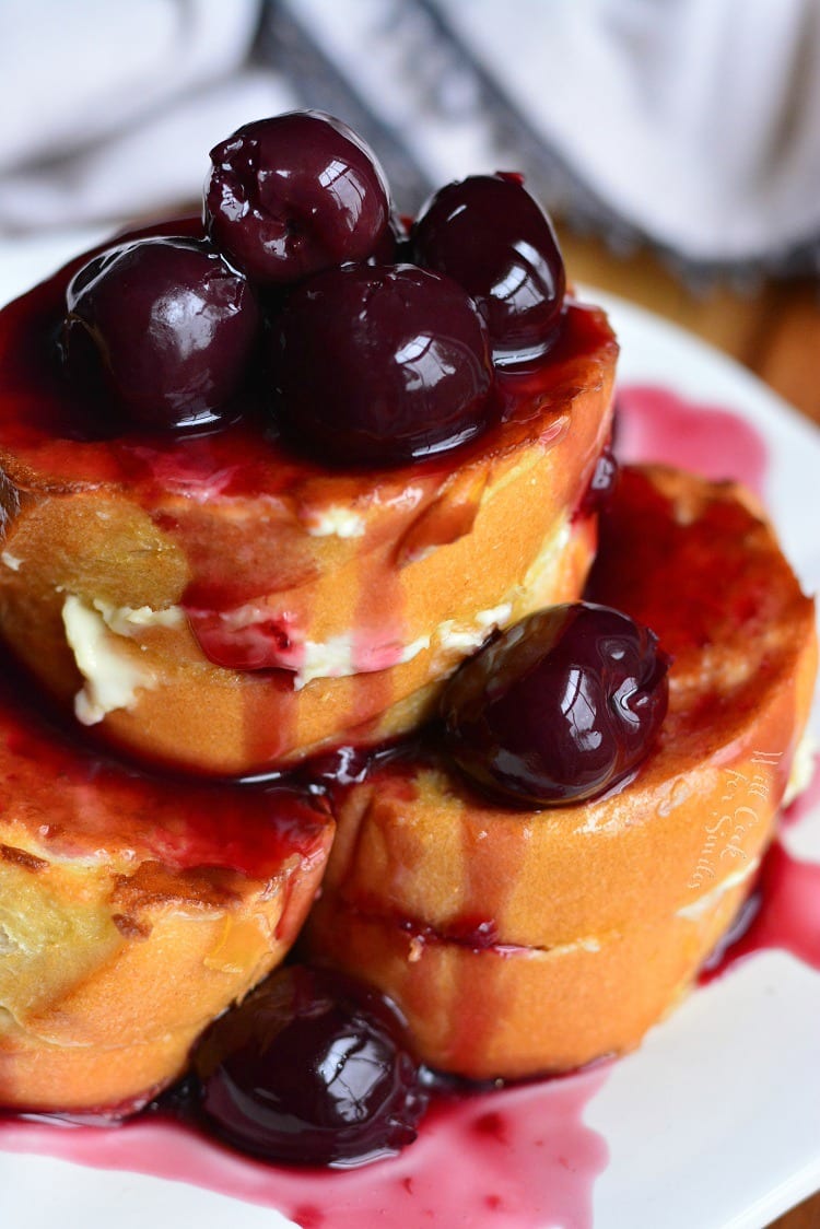 cherry cheesecake with cherries all over the top stacked on a white plate.