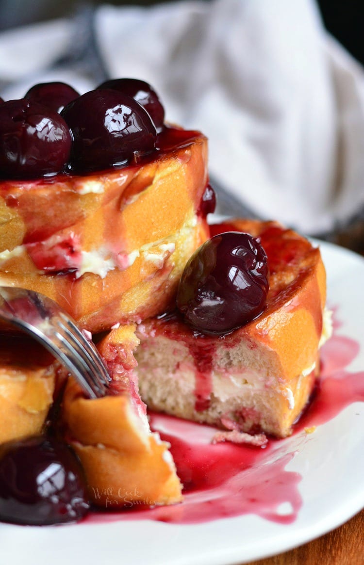 Cherry french toast with cherries on top and a slice cut out of it.