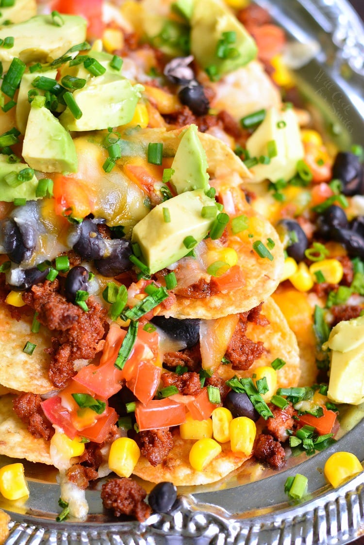 closeup of nachos in a silver dish with dice avocado on top