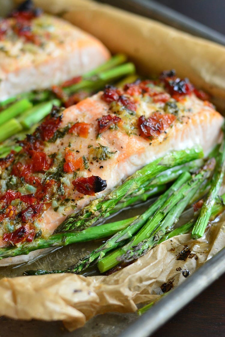 baked salmon with sun dried tomatoes and asparagus in sauce in a baking dish.