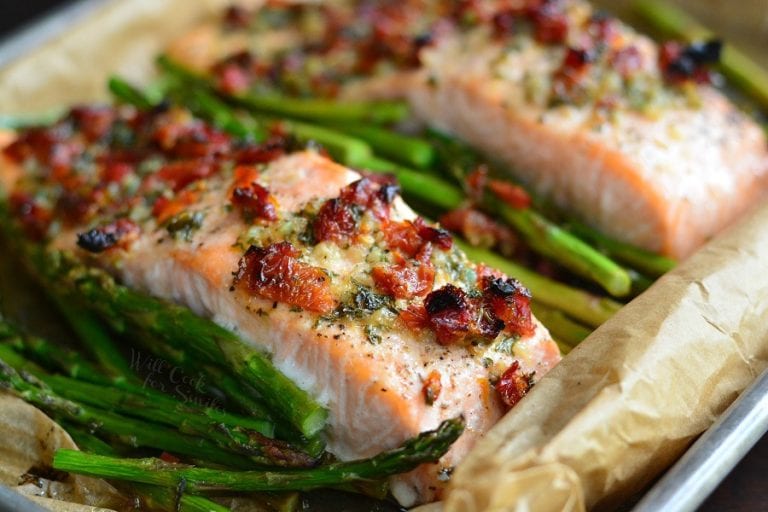 two baked salmon filets in baking pan with sun dried tomatoes and asparagus.