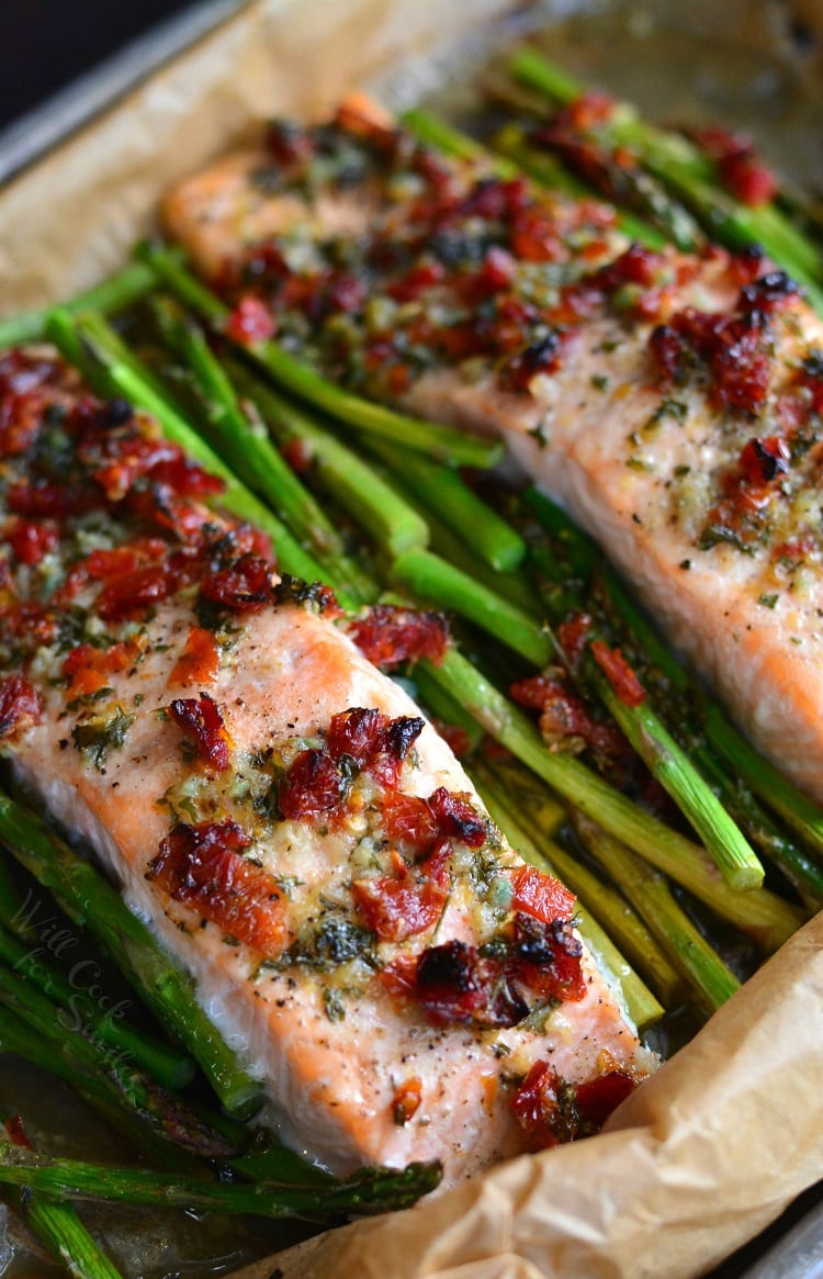 two salmon filets on a baking sheet with asparagus and sun dried tomatoes.