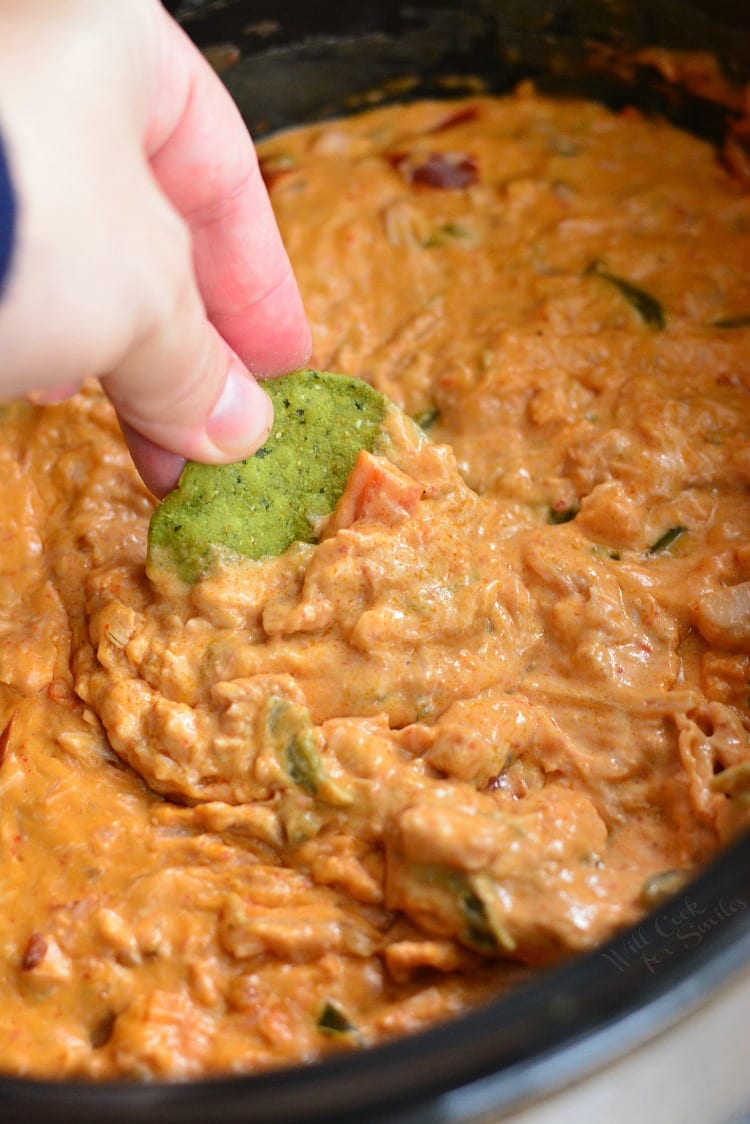 dipping a green tortilla chip into the enchilada dip.