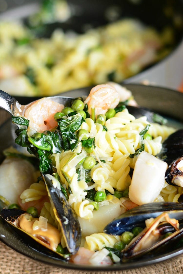 Creamy Spinach and Peas Seafood Pasta in a pan with a spoon lifting some out 