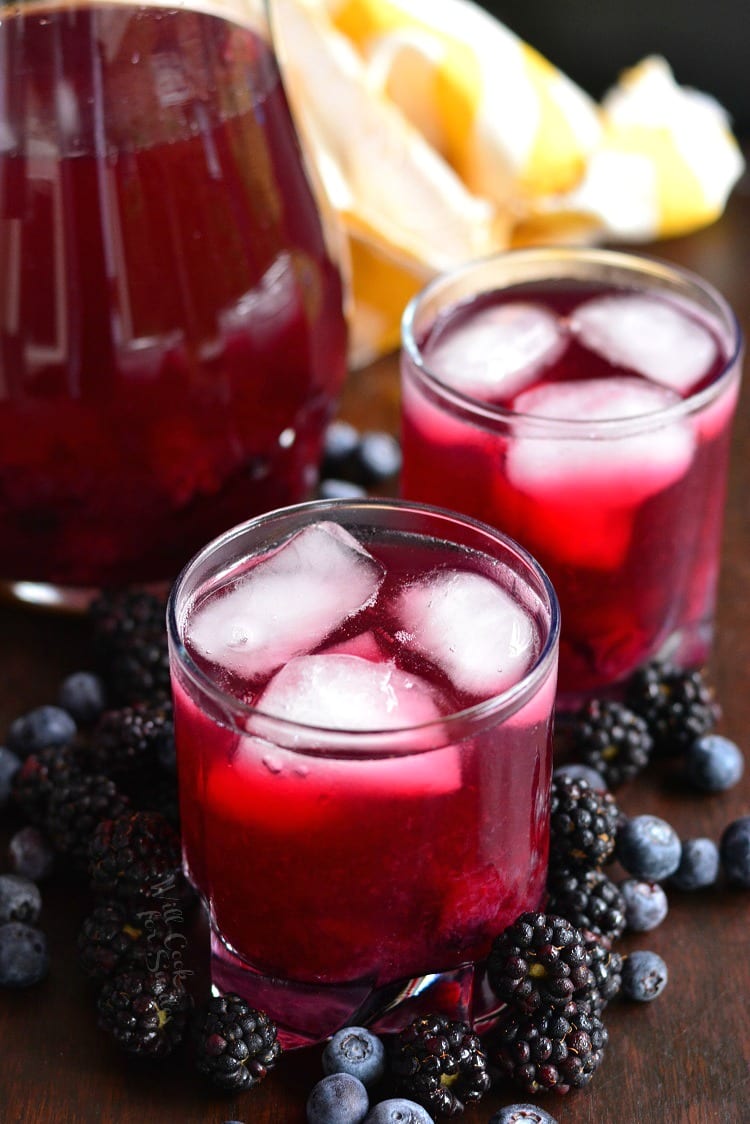 two glasses of Blueberry Blackberry Iced Green Tea on a wood table with a pitcher 