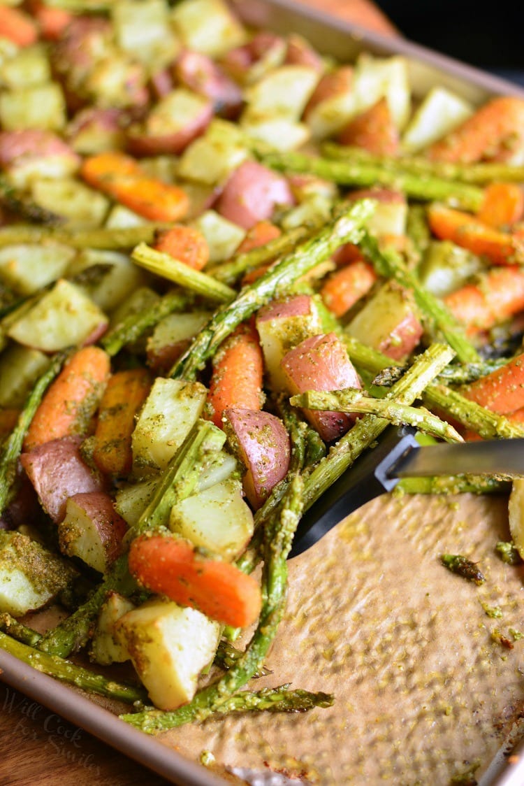 Pesto Roasted Potatoes Carrots and Asparagus on a baking sheet  with a spatula 