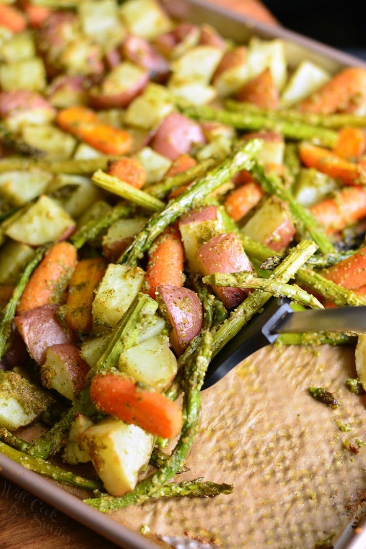 Pesto Roasted Potatoes Carrots and Asparagus on a baking sheet with a spatula 