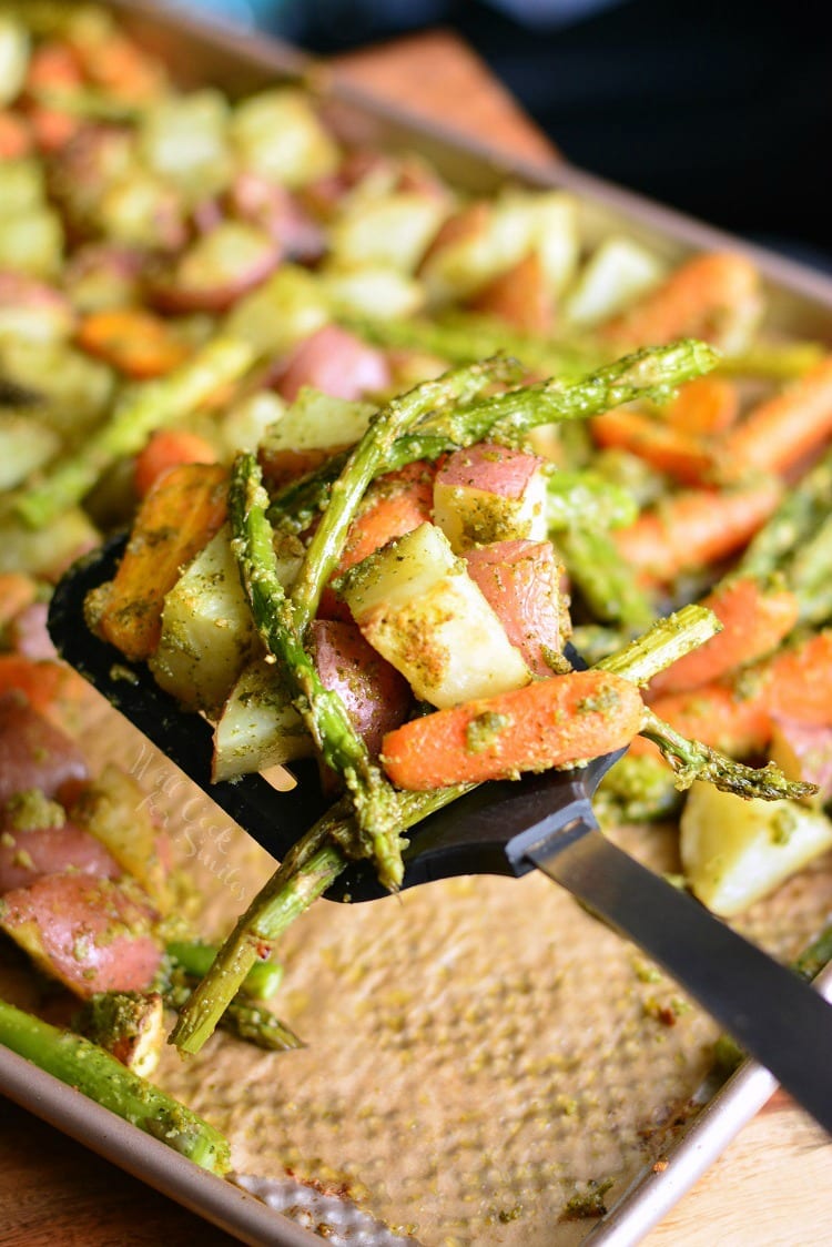 Pesto Roasted Potatoes Carrots and Asparagus on a baking sheet with a spatula lifting some out 