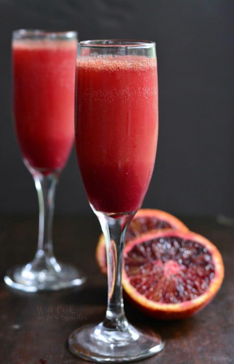 side view of deep red mimosa in a glass with blood orange cut in half next to it