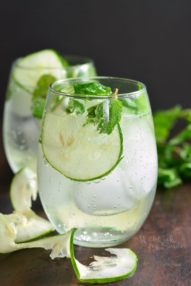 side view of gin cocktail with slices of cucumber and mint. Slice of cucumber next to the glass too