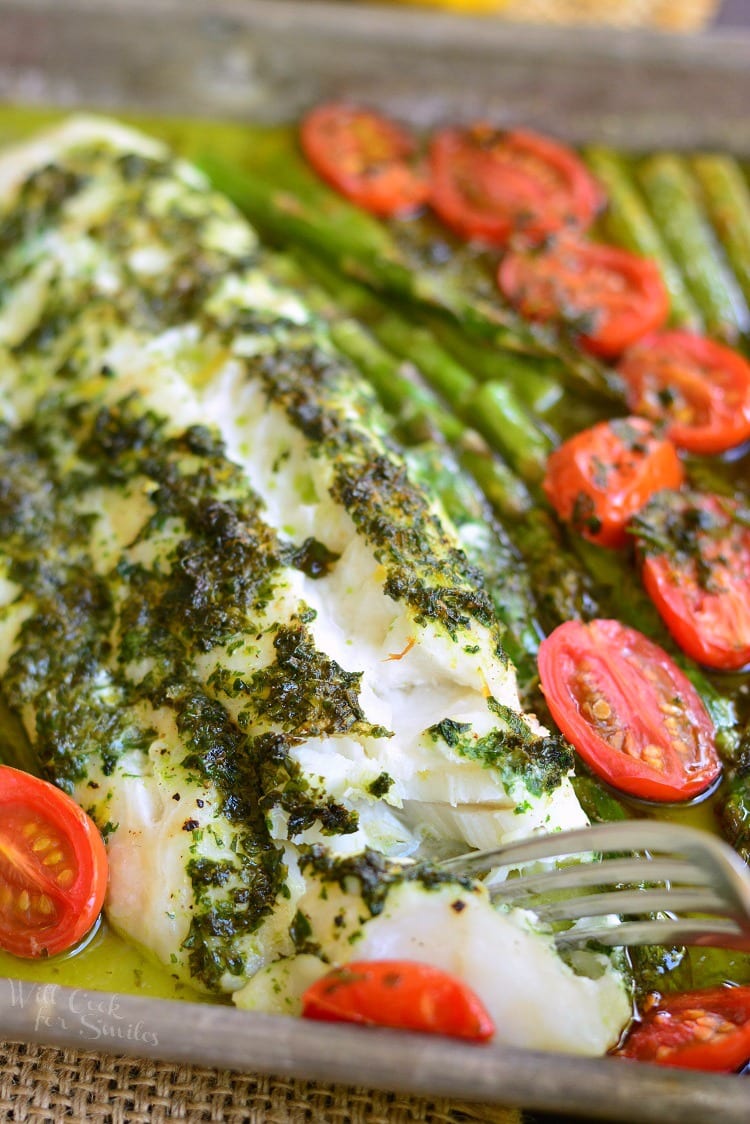 Lemon Herb Butter Cod with Asparagus and Tomatoes in a baking dish with a fork 