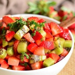 strawberry and kiwi in a fruit salad with mint on top.