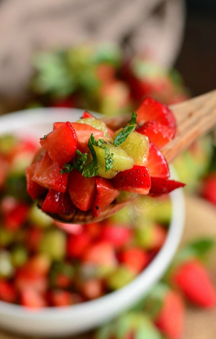 spoon full strawberry and kiwi fruit salad with the rest of it in a white bowl.